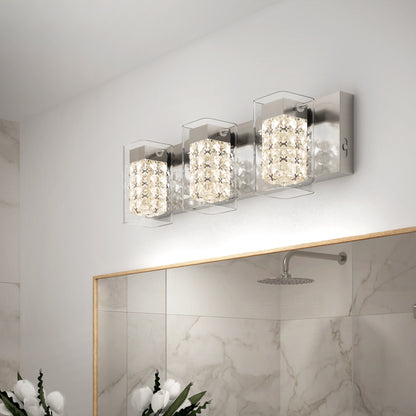 The Artika Crystal Cube LED bathroom vanity light 5 CCT features three crystal-like square lights above a large mirror, reflecting marble-patterned walls and a rainfall showerhead. White flowers sit in the bottom left corner.