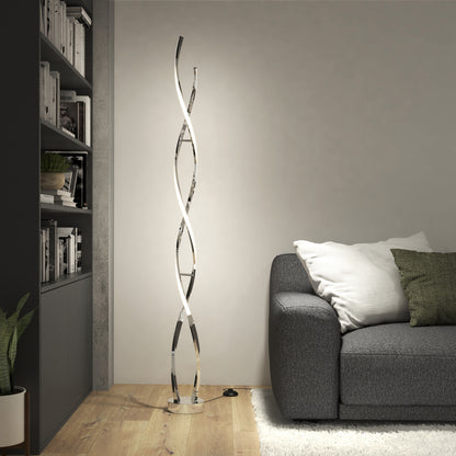A modern living room features a gray couch with white and green pillows, a bookshelf, a potted plant on wooden flooring, and the Artika Swirl modern LED floor lamp beside a light-colored wall.