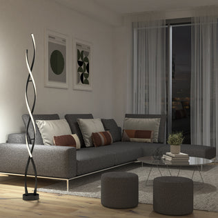 Modern living room with a gray sectional, abstract art, Artika Swirl LED floor lamp, round ottomans, and a glass coffee table.