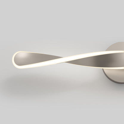 The Artika Finley LED modern bathroom vanity light 3 CCT features a sleek, metallic infinity loop design with a soft white glow, mounted on a round base against a plain light gray background.