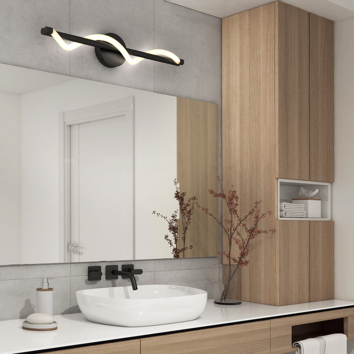 Modern bathroom with a rectangular mirror above a white sink, matte black faucet, light wood cabinets, a decorative branch in a vase, soap dispenser, and a curved LED light fixture mounted above the mirror.