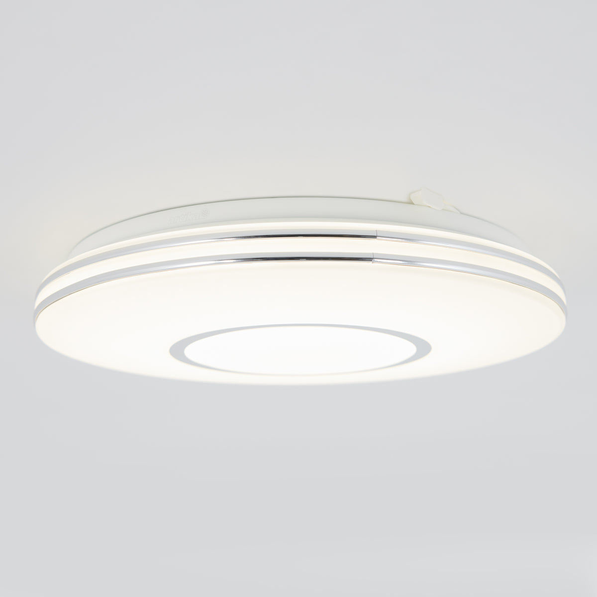 A modern, round ceiling light fixture with a white and silver design, emitting a bright, even glow against a plain light gray ceiling.