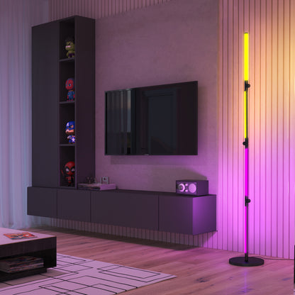 A modern living room features light wood floors, vertical wall panels, a wall-mounted TV, shelves with superhero figures, a floating cabinet, and the Artika Fitch smart foldable RGB LED gaming floor lamp glowing yellow and pink in the corner.