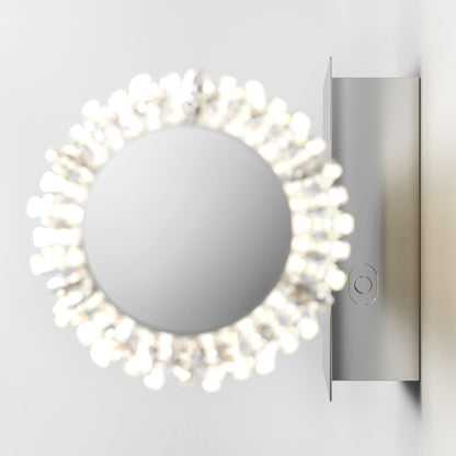 The Artika Exalto LED bathroom vanity light features a round wall-mounted mirror with a decorative frame of small lights, attached to a rectangular metal base on a white wall.