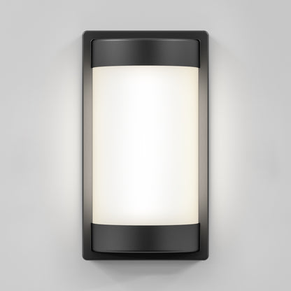 The Artika Fogo modern LED indoor-outdoor wall light 5 CCT features a frosted cylindrical glass panel and black metal frame, casting a soft white glow against a light gray wall.