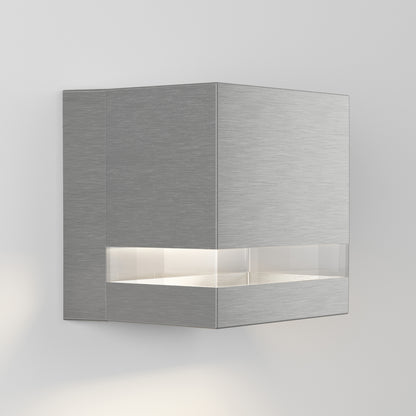 The Artika Valor Square LED indoor-outdoor wall light features a modern, square metallic design with a brushed finish and a horizontal frosted strip that emits soft white light, shown mounted on a plain light-colored wall.