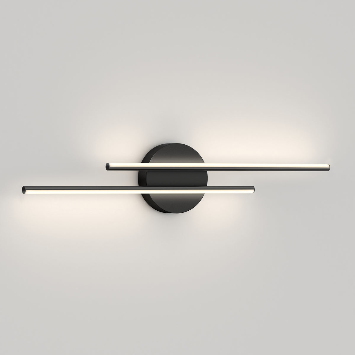 A modern wall sconce with a black circular base and two parallel horizontal light bars extending outward, emitting soft white light against a plain light gray wall.