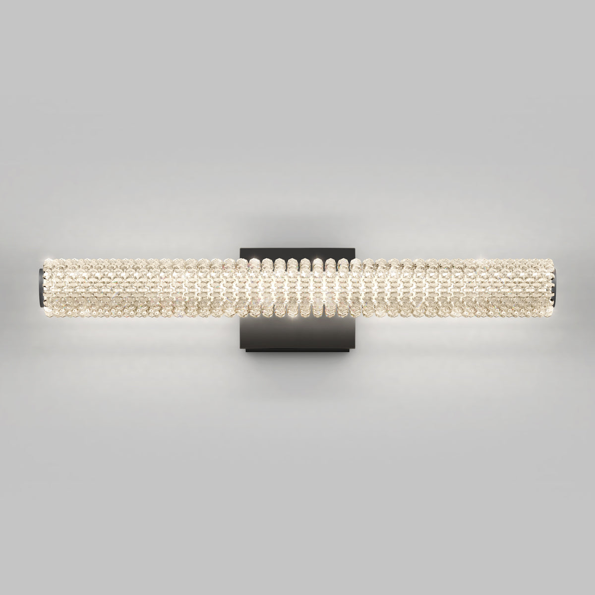 Wall-mounted light fixture with a cylindrical shade made of rows of clear crystal beads on a black rectangular base, against a plain gray background. The light is turned on, emitting a soft glow.