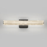 Wall-mounted light fixture with a cylindrical shade made of rows of clear crystal beads on a black rectangular base, against a plain gray background. The light is turned on, emitting a soft glow.