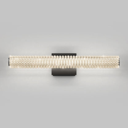 The Artika Exalto LED bathroom vanity light features a horizontal cylindrical shade with clear crystal-like beads on a rectangular black base, providing soft, even illumination.