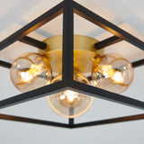 Close-up of a modern ceiling light fixture with a geometric black metal frame, gold center, and exposed round bulbs glowing warmly.