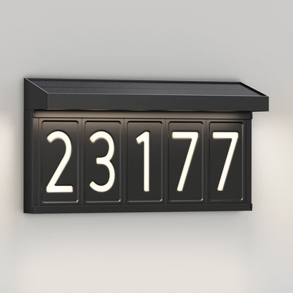 The Artika Bowen solar LED outdoor address wall light 5 CCT is a black rectangular plaque with illuminated white numbers "23177," a slanted top, and maintenance-free lighting for clear visibility, mounted on a light-colored wall.