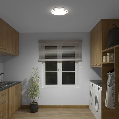 A laundry room with wooden cabinets, side-by-side washer and dryer, sink, potted plant, and window with blinds illuminated by the Artika Emina 13 in. LED flush mount light (3 CCT, 800 lumens).