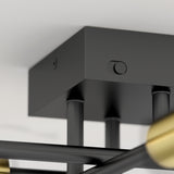 Close-up of a modern black ceiling light fixture with a square mounting plate, three cylindrical rods, and part of a gold accent visible on one rod. The fixture is attached to a white ceiling.