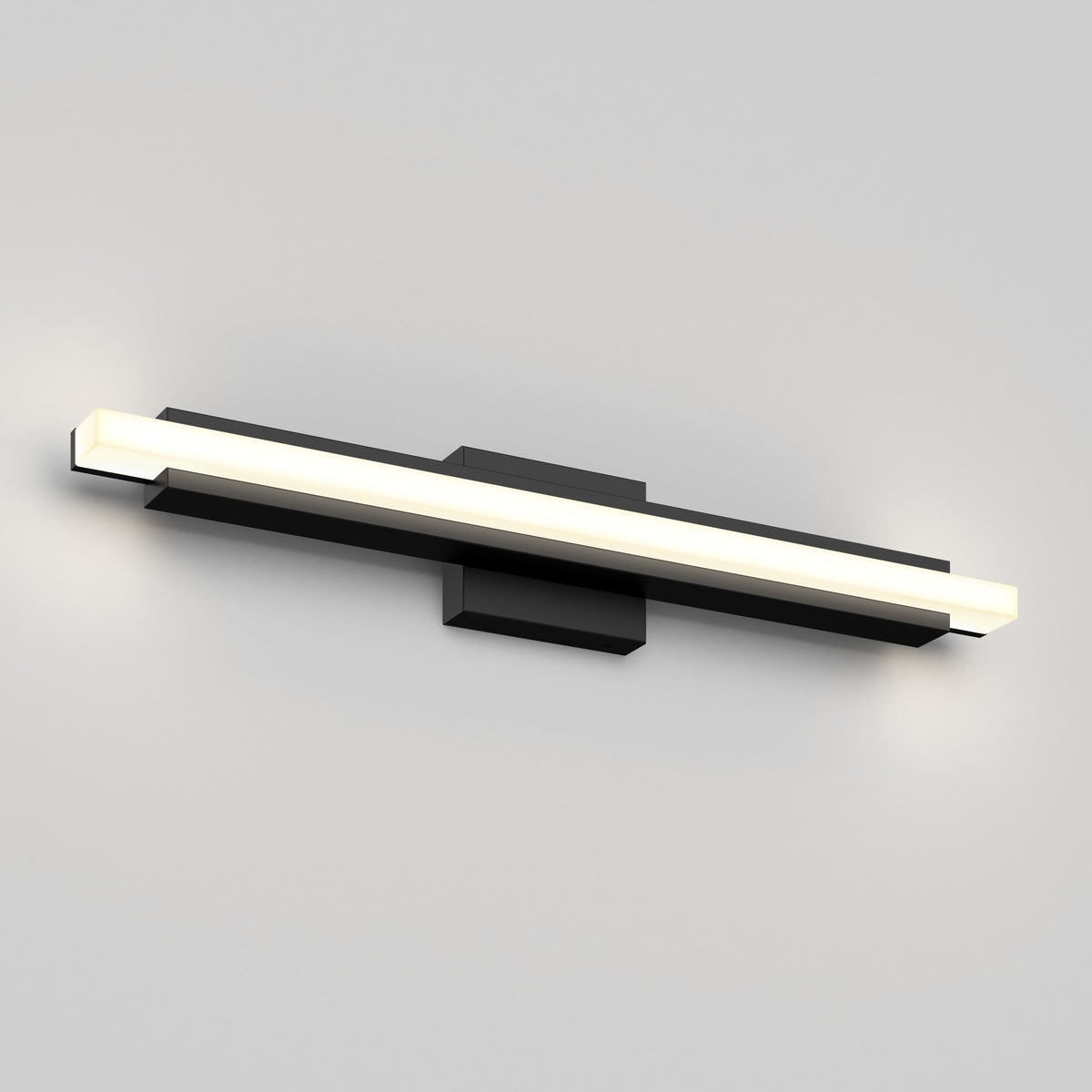 A modern wall-mounted LED light fixture with a horizontal, rectangular design in black and white, emitting a soft glow at both ends against a plain light gray wall.