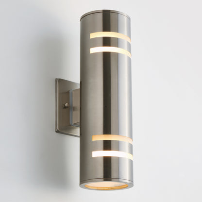 The Artika Voltz indoor-outdoor wall light is a modern cylindrical sconce with a brushed metal finish, mounted on a square base. It has horizontal cutouts shining warm light from top and bottom, shown against a plain white background.