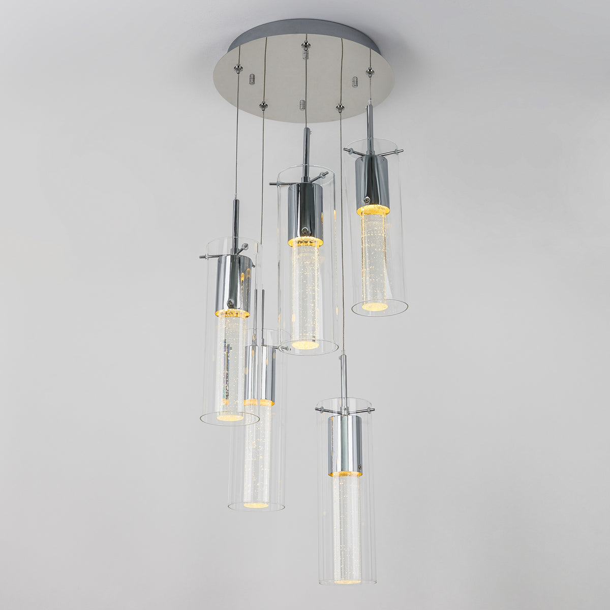 The Artika Essence 5-light LED pendant features five cylindrical glass shades suspended at varying heights from a round metallic base, each illuminated with an energy-efficient LED.