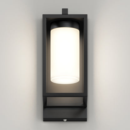 The Artika Aurel Outdoor LED Light, 3CCT, features a modern black rectangular frame with a cylindrical frosted glass fixture, mounted on a light gray wall and emitting a soft, even glow.