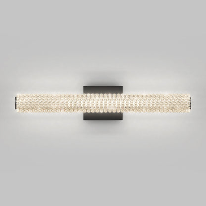 The Artika Exalto LED bathroom vanity light features a modern rectangular black base and a horizontal cylindrical fixture with crystal-like beads, casting a soft, diffuse glow—perfect for any contemporary space.