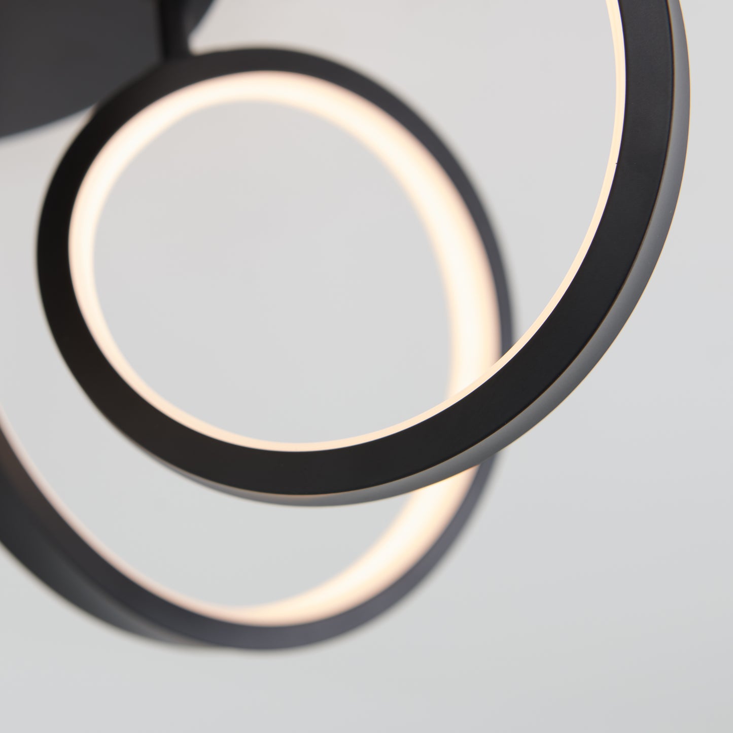 Close-up of the Artika Swirl Ribbon flush mount light, featuring two intersecting black rings illuminated along their inner edges against a neutral background.