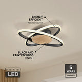 Modern ceiling light fixture with two LED rings and a wooden center. Text highlights energy efficiency, black and painted wood finish, integrated LED, and a 5-year warranty. The fixture is mounted on a beige ceiling.