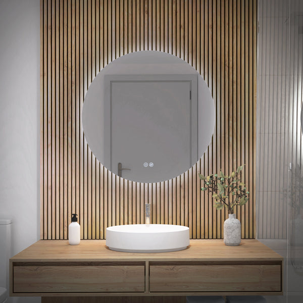 A modern bathroom features the Artika-CAN-dev Raya 24 in. LED mirror 3 CCT with defogger above a circular white sink on a wooden vanity, alongside a soap dispenser and vase with green branches. A closed door is reflected in the mirror.
