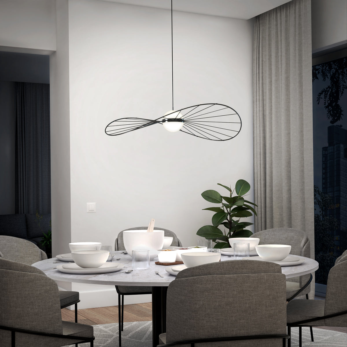 A modern dining room features a round marble table with gray upholstered chairs. Overhead, the Artika Tolena LED pendant light 3 CCT adds style, while a green plant sits by tall gray curtains.