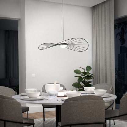 A modern dining room features a round marble table with gray upholstered chairs. Overhead, the Artika Tolena LED pendant light 3 CCT adds style, while a green plant sits by tall gray curtains.