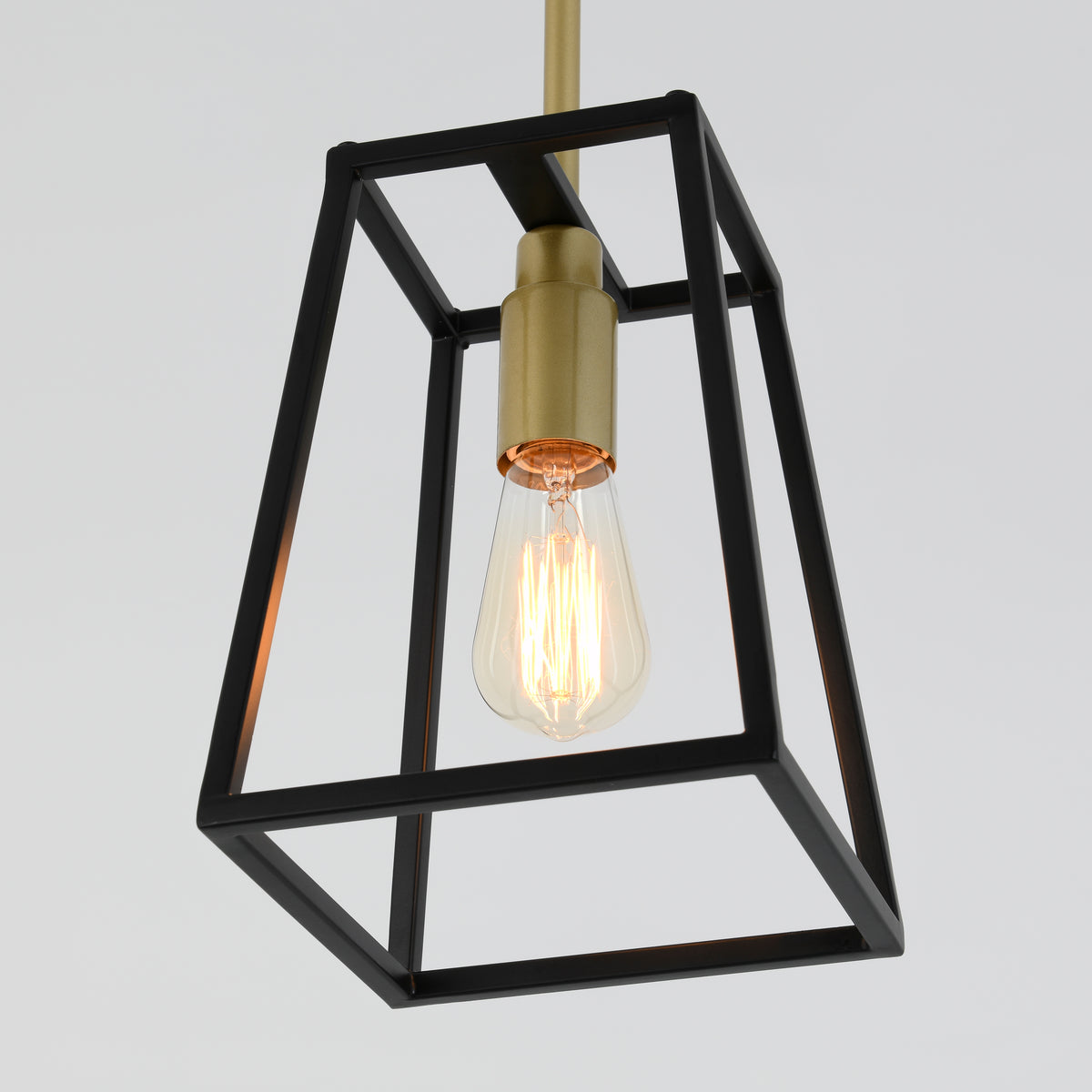 A hanging pendant light with an exposed vintage-style bulb, encased in a geometric black metal frame and gold fixture, against a plain light background.