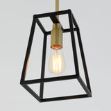 A hanging pendant light with an exposed vintage-style bulb, encased in a geometric black metal frame and gold fixture, against a plain light background.