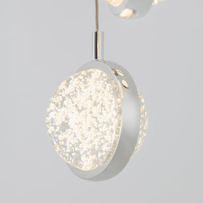 The Artika Avalon 4-light LED pendant features a modern round clear glass shade with bubbles, emits a bright white glow, and hangs from a metallic cord against a plain light gray background.