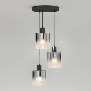 The Artika Haze modern 3-light pendant features cylindrical glass shades hanging at varied lengths from a round black mount, each showcasing a visible bulb, set against a plain light gray background.