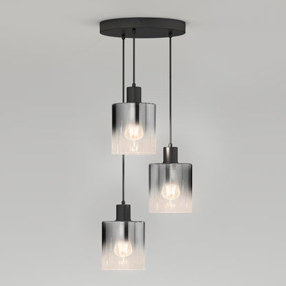 The Artika Haze modern 3-light pendant features cylindrical glass shades hanging at varied lengths from a round black mount, each showcasing a visible bulb, set against a plain light gray background.