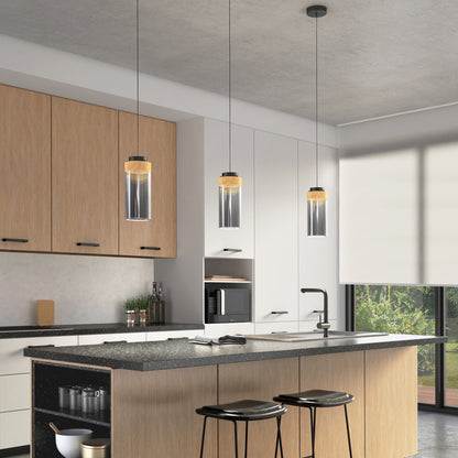 Modern kitchen with light wood cabinets, a large island with black countertop, two black stools, three Artika Hanson 1-light LED pendant lights above, and a large window with a roller shade letting in natural light.
