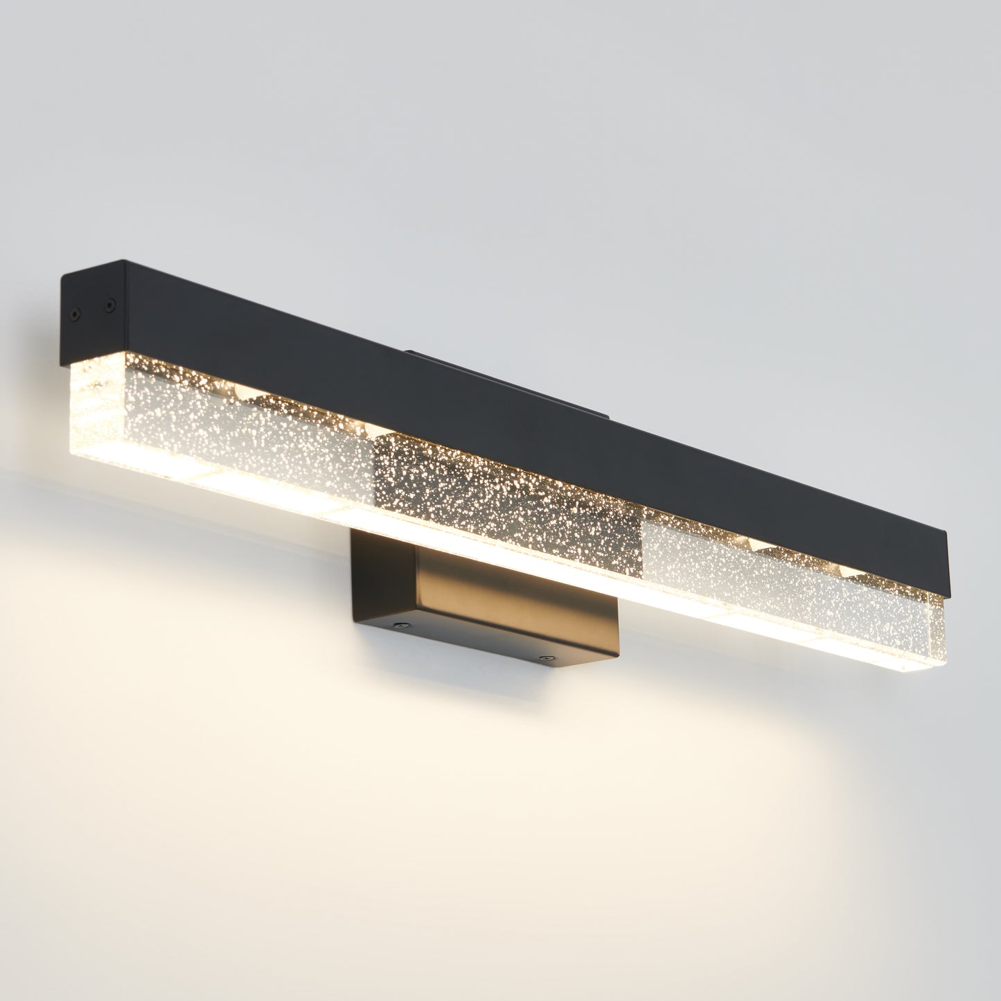 The Artika Bubble Bar LED bathroom vanity light features a rectangular black frame and textured illuminated glass bar, casting soft white light on a light-colored wall.