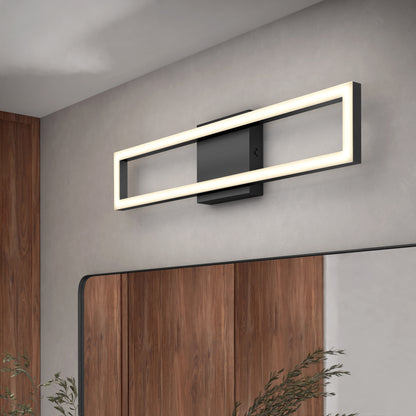 The Artika Dover modern LED bathroom vanity light 5 CCT, featuring a rectangular black base and glowing frame, is mounted above a mirror on a light gray wall, with wood paneling and green plants below.