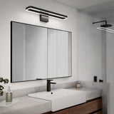 Modern bathroom with a large rectangular mirror, an illuminated light fixture above it, a white sink with a black faucet, wooden cabinets, and a glass shower with a rainfall showerhead in the background.