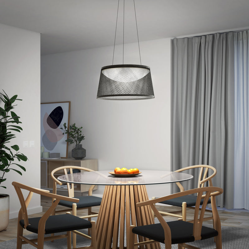 A modern dining area with a glass table, four wooden chairs with black cushions, a bowl of oranges, a plant, framed art, grey curtains over the window, and an Artika Adrian LED pendant light 3 CCT illuminating the space.