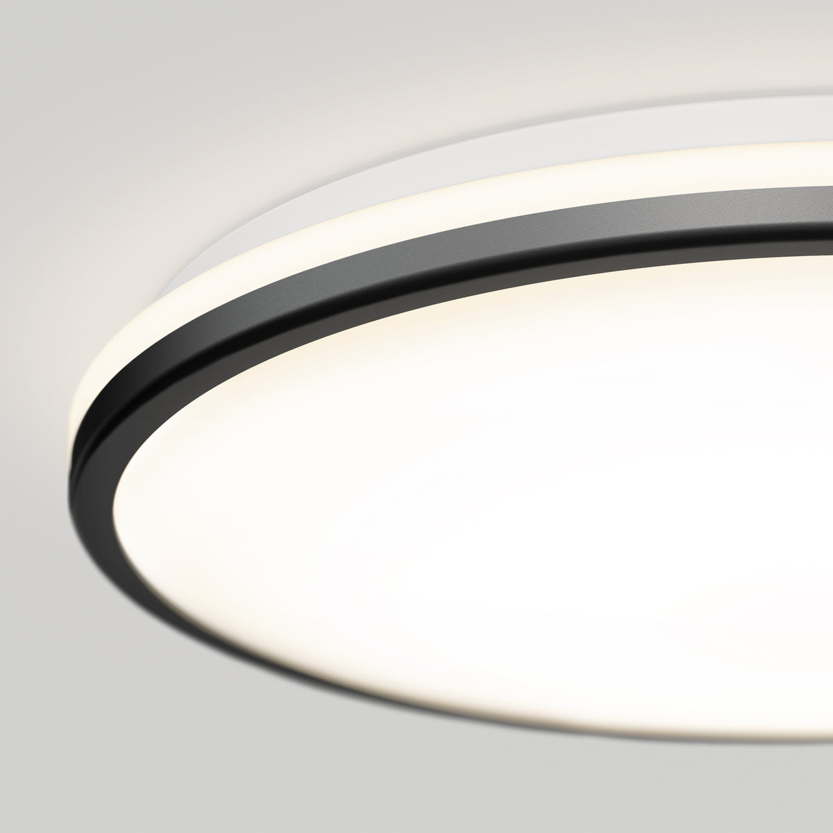 Close-up of a modern, round ceiling light fixture with a white diffuser and a black outer ring, illuminated against a light gray ceiling.