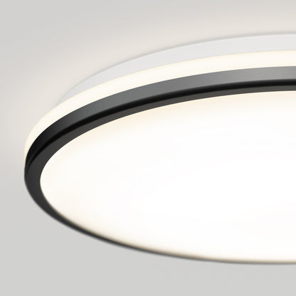 Close-up of the Artika Macy 15 in. LED modern flush mount light, featuring a circular design with a white diffuser and black trim, emitting a soft glow on a light gray ceiling. RGB Wifi-enabled for customizable lighting.
