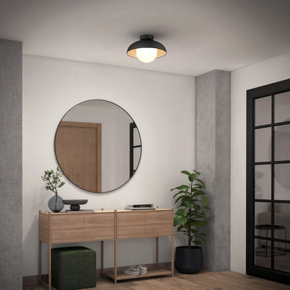 A modern entryway with a wood console table, round mirror, potted plant, and green ottoman. A black-framed glass door and the Artika Boden LED flush mount light 5 CCT complete the minimalist decor.