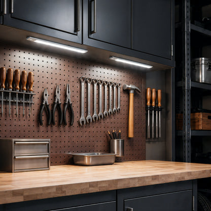 Two Artika Outline under cabinet LED light 3CCT panels mounted under cabinets, illuminating a workbench with tools hanging on a pegboard.