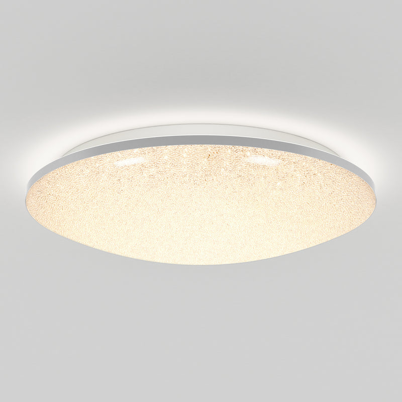 The Artika Sparkle LED flush mount light features a round, textured surface and emits a warm, even glow. Mounted on a white ceiling, this modern fixture comes with a remote for easy control.