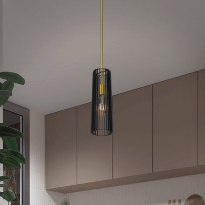 The Artika Gatsby Mini modern mid-century pendant light, featuring a black cylindrical cage shade and gold fixture, hangs in a contemporary kitchen with beige cabinets and a large green plant nearby.
