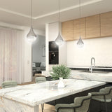 Modern kitchen with a marble island, gray chairs, a white vase with green foliage, pendant lights, wood cabinets, and a hexagon tile backsplash. A cozy living area with a sofa is visible in the background.