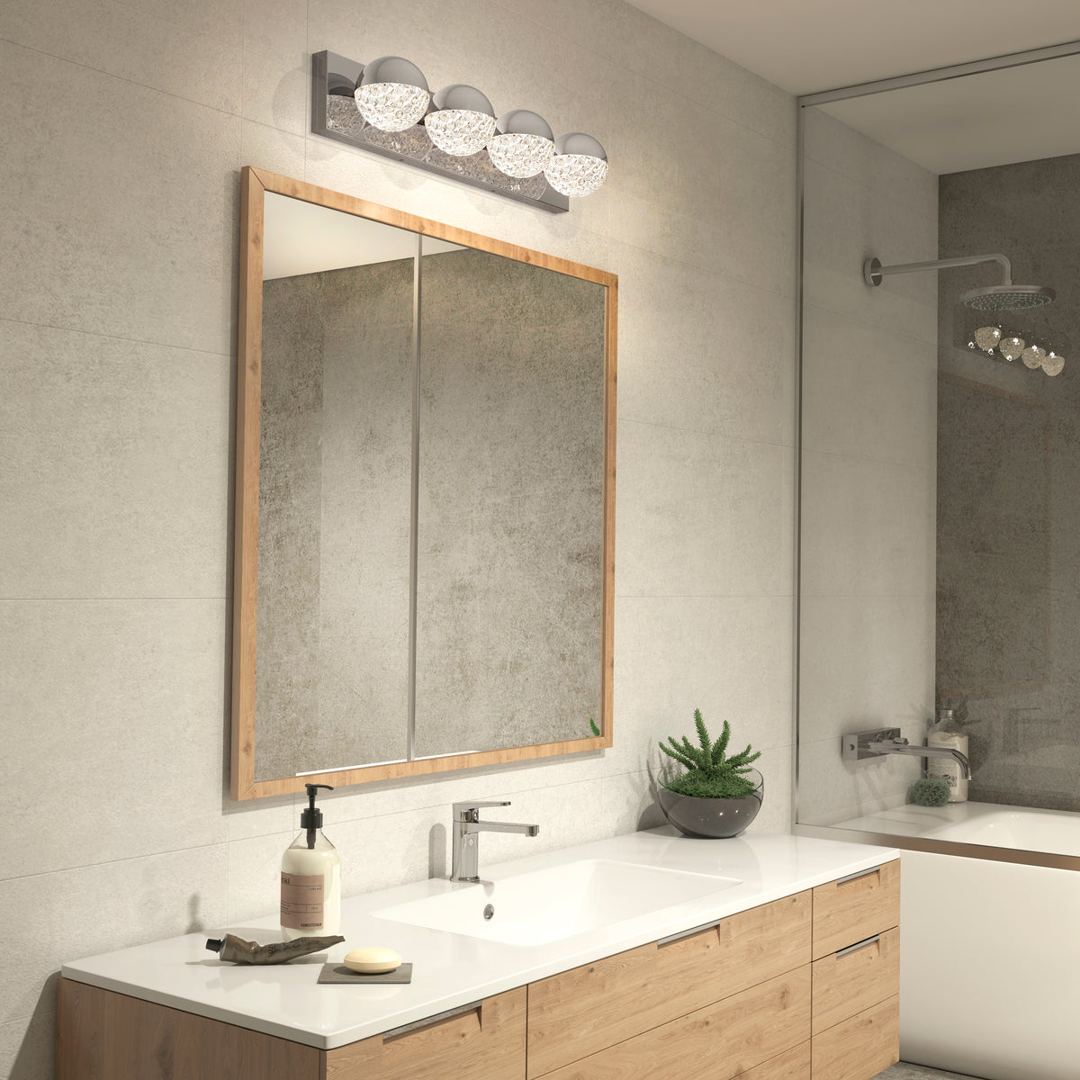 Modern bathroom with a large wood-framed mirror above a white countertop, single sink, soap dispenser, small plant, and a row of decorative lights above the mirror. A shower is visible in the reflection.