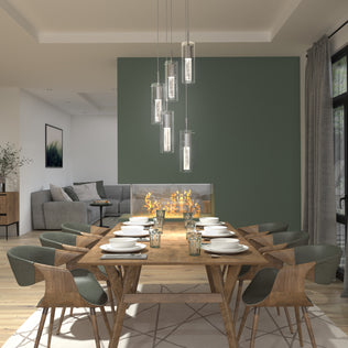 A modern dining room with a wooden table for eight, green upholstered chairs, the Artika Bubble Swirl 5-light pendant overhead, and a glass-enclosed fireplace; gray sofa visible in the living area.