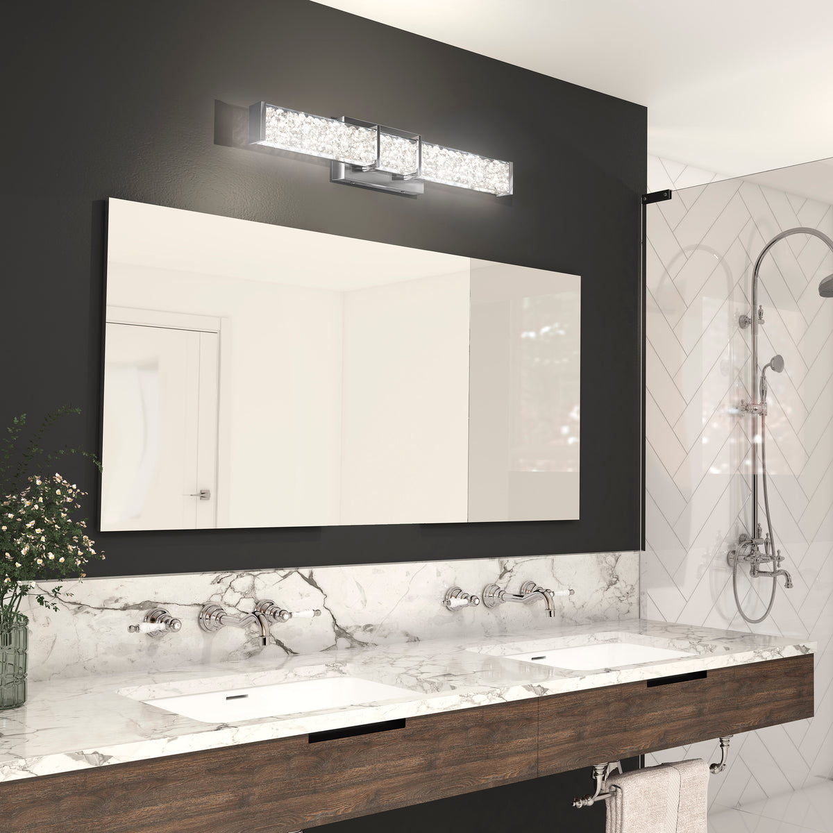 A modern bathroom with a marble countertop, two sinks, a large mirror, a sleek wall-mounted light fixture above the mirror, dark accent wall, and a glass-enclosed shower with chrome fixtures.