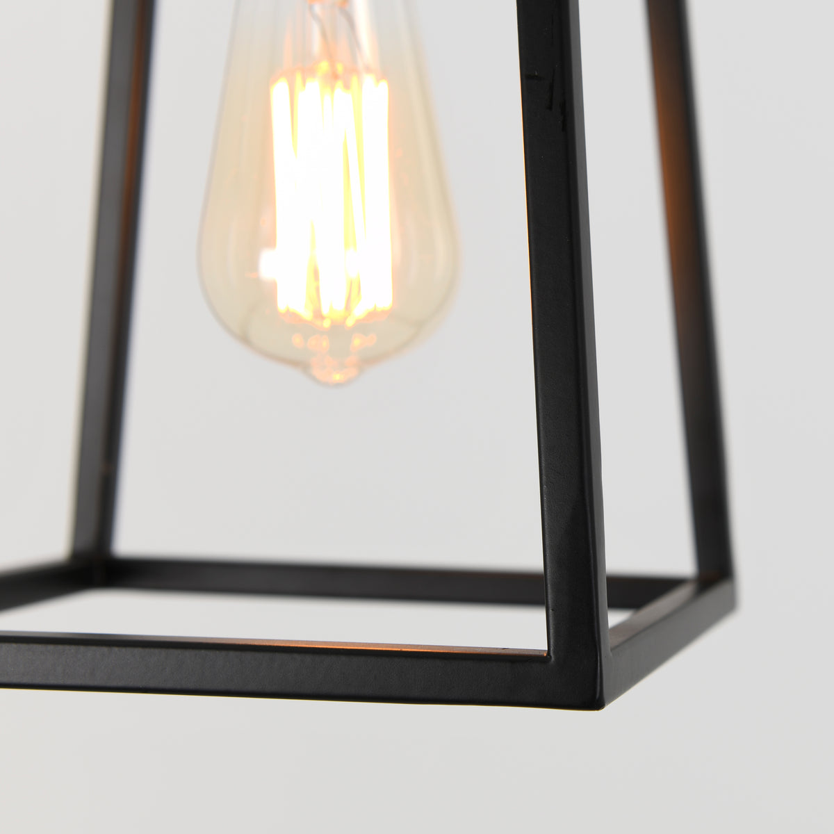 A close-up of a glowing vintage-style light bulb inside a minimalist black metal frame against a plain light background.