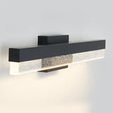 A modern wall-mounted light fixture with a rectangular black frame and a clear section featuring small bubble-like patterns, emitting a soft, warm glow against a light-colored wall.